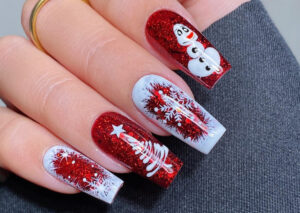 A close up shot of a hand with festive acrylic nails, showcasing a glittery red polish with white Christmas motifs. The details on each nail include a snowman, tree, and snowflakes.